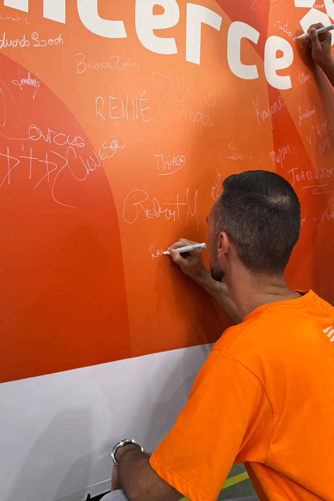 Colaborador da Alicerce assinando o painel da marca, já coberto de assinaturas do time, no evento de lançamento